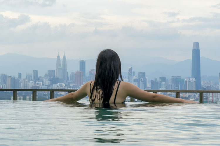 Rear view of woman looking at swimming pool against buildings in city