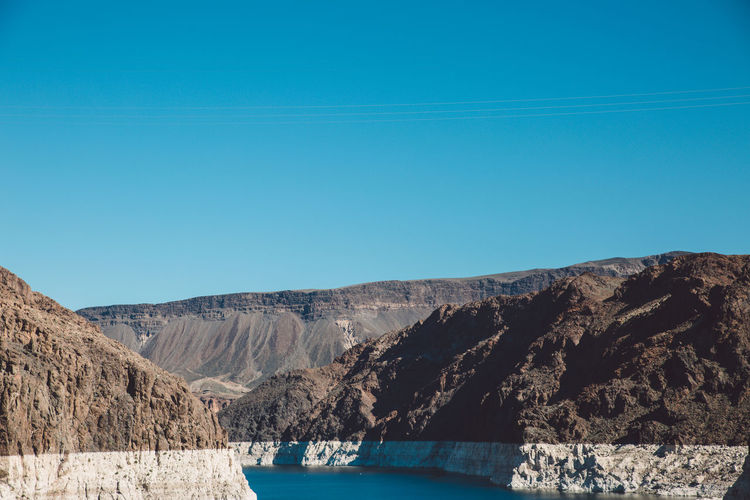 Colorado river amidst mountain at hoover dam against clear blue sky