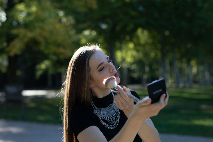 Young woman applying face powder on road