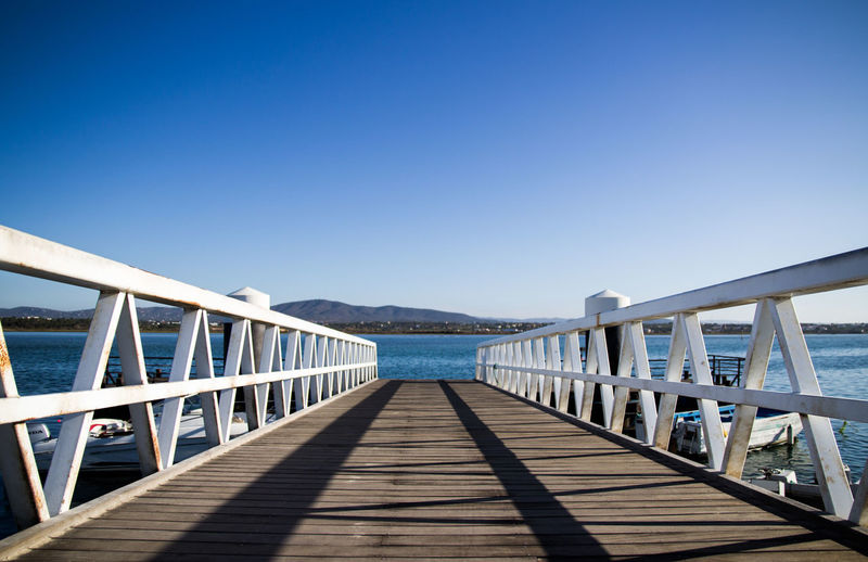 Footbridge over pier against clear blue sky