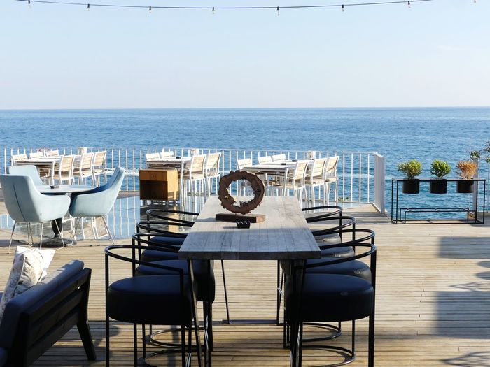 Chairs and tables at restaurant by sea against sky