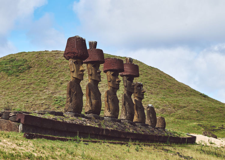 View of moai statues on mountain against cloudy sky