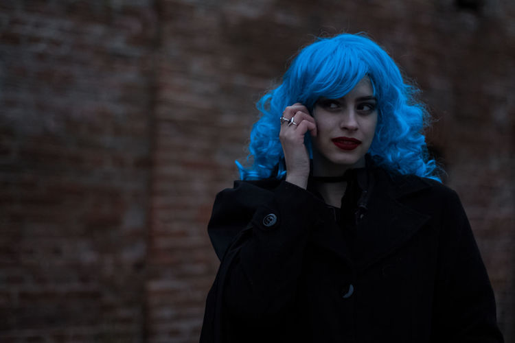 Woman wearing blue wig against brick wall