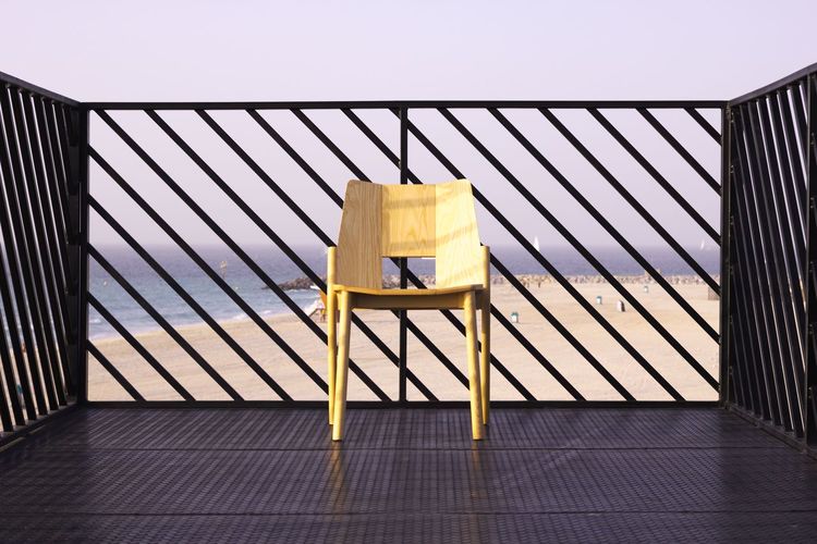 Close-up of chair on by fence against sea