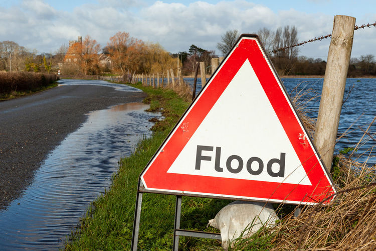 Flood triangular warning sign on road flooded by river that has burst is banks with selective focus 