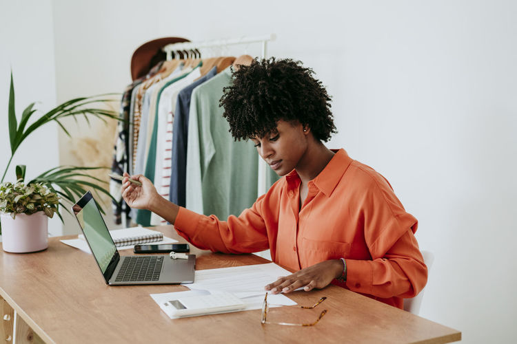 Freelancer sitting with laptop and examining financial bills at desk