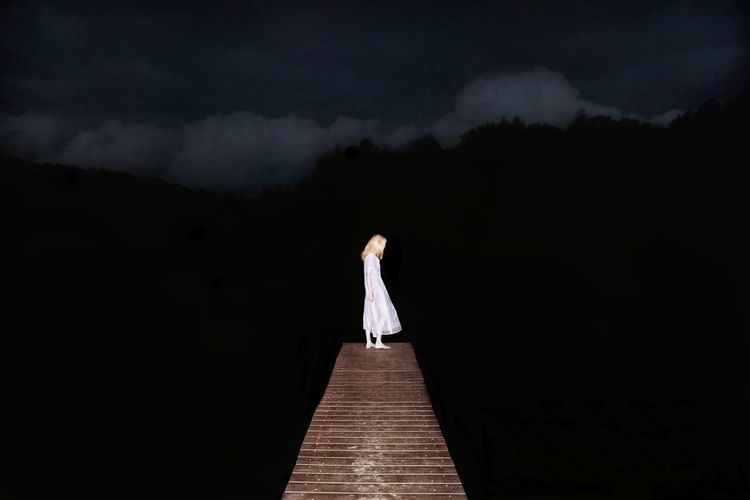 Woman standing on pier over lake at night