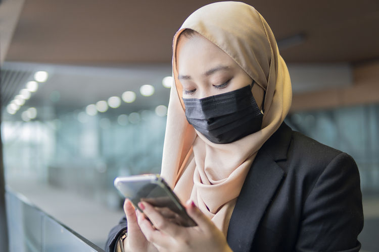Malay woman wearing face mask executive outdoor using smart phone