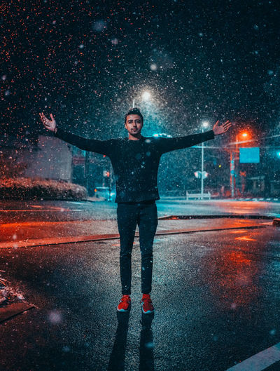 Full length of man with arms outstretched standing on street during snowfall