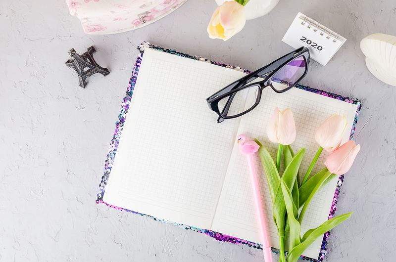 Feminine styled work place with tulips, eyeglass and notebook.
