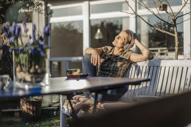 Woman wearing headphones relaxing on garden bench