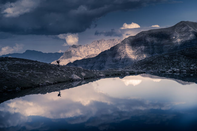 Alpine lake with cloudy sky and trekker reflecting on watee