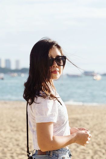 Portrait of beautiful woman standing at beach against sky