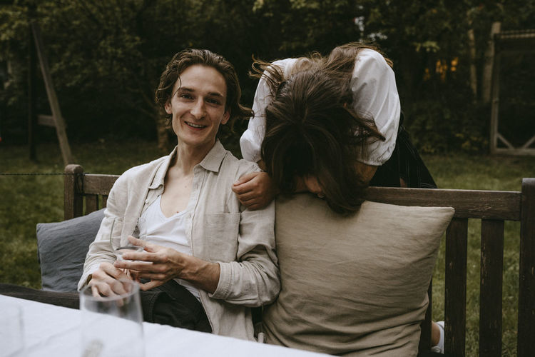 Smiling male by female friend sitting on bench during social gathering