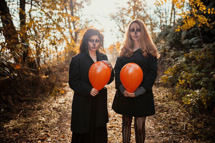 Friends with spooky make-up and costume holding balloon while standing on forest path