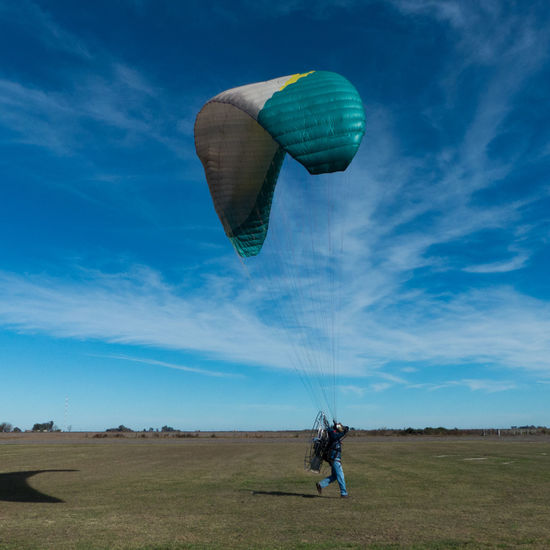 Side view of man with electric motor and parachute running on land while paragliding against sky