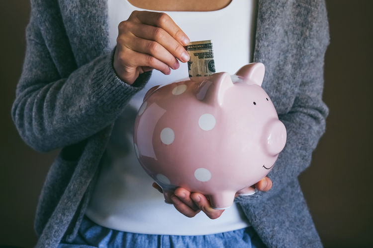 Woman putting bill in happy piggy bank. saving money for household payments. economic crisis concept