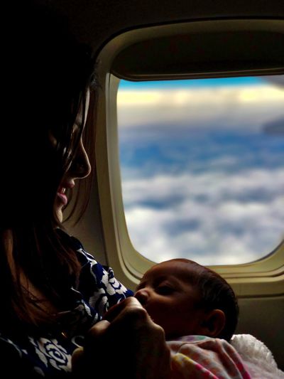 Close-up of woman breastfeeding baby girl by airplane window