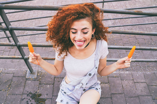 High angle view of happy woman having orange popsicles on footpath