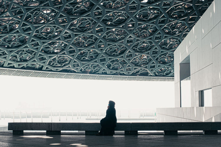 Side view of woman sitting on window of building