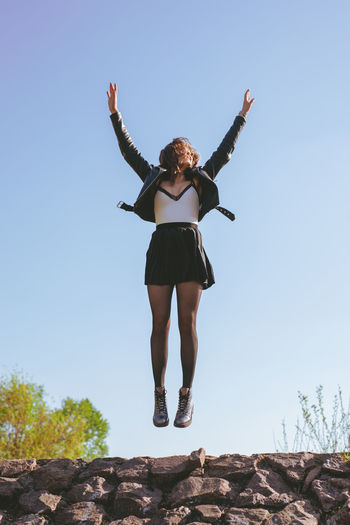 Low angle view of woman levitating against clear sky