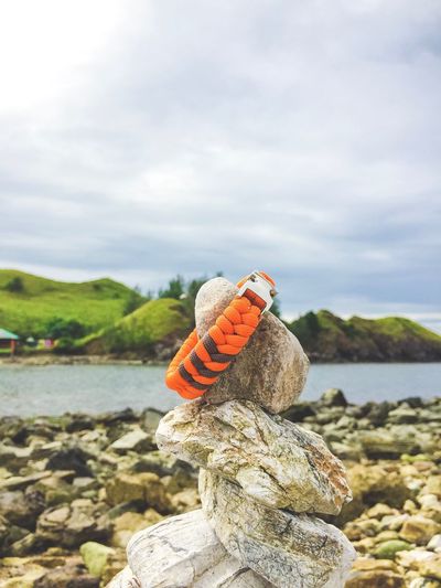 A stylish and trendy travel paracord bracelet on a stack of pebbles by the shore under a cloudy sky.