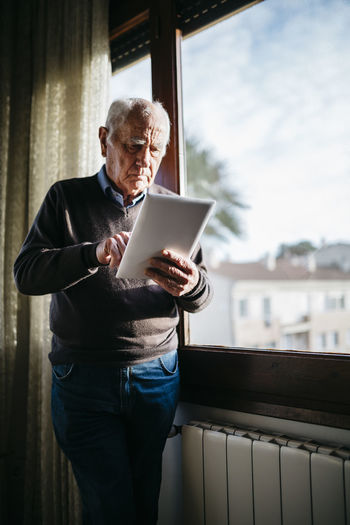 Side view of man using digital tablet while standing at home