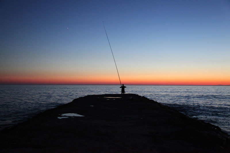 Silhouette man fishing in sea against sunset sky, portugal 