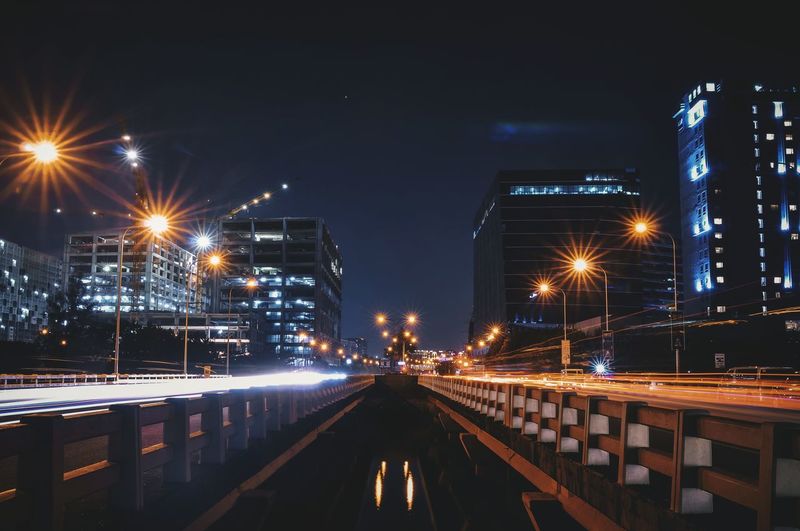 Illuminated street lights in city against sky at night