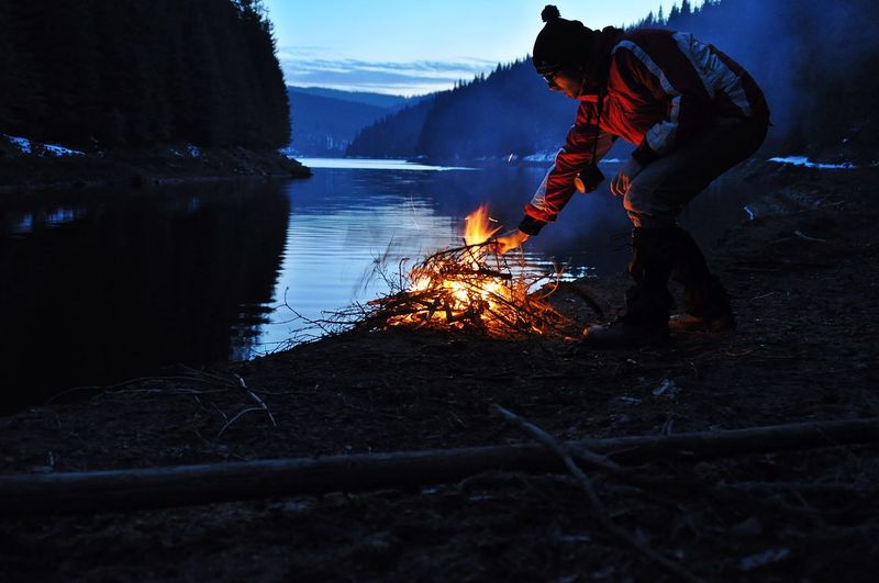 Man burning bonfire at lakeshore during dusk