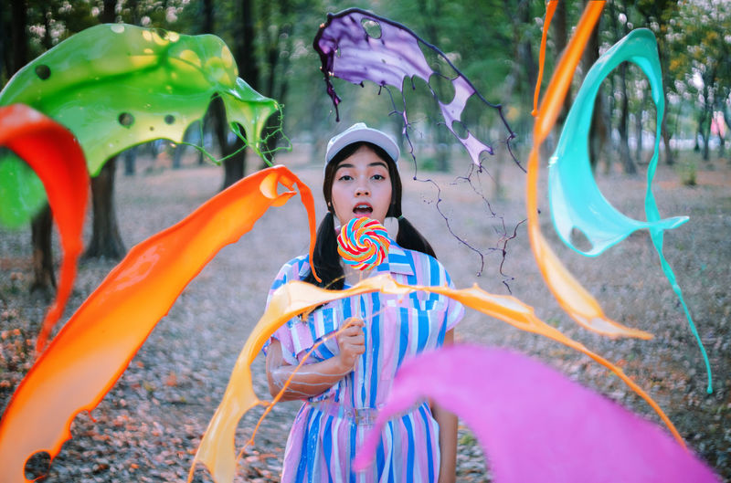 Multi colored paint thrown on woman holding candy in forest