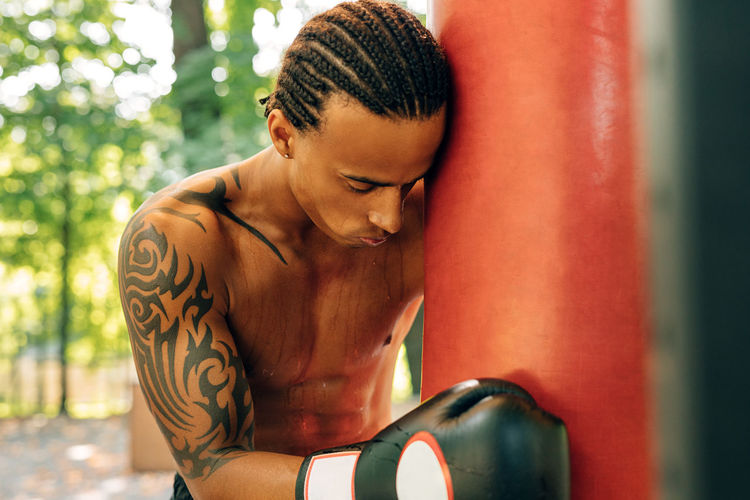 Tied athlete leaning on punching bag outdoors