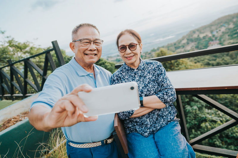 Portrait of couple taking selfie while standing by railing