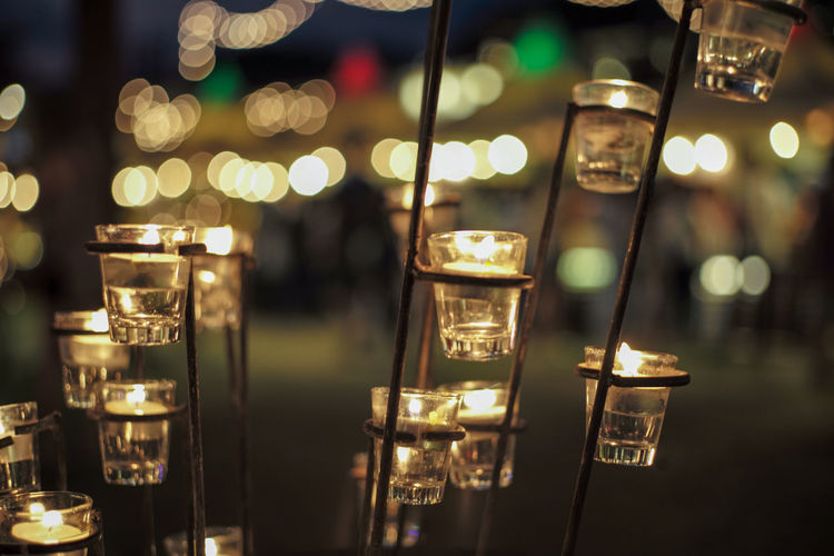 Close-up candle in small glass jars in the steel holder with blurred bokeh lights background