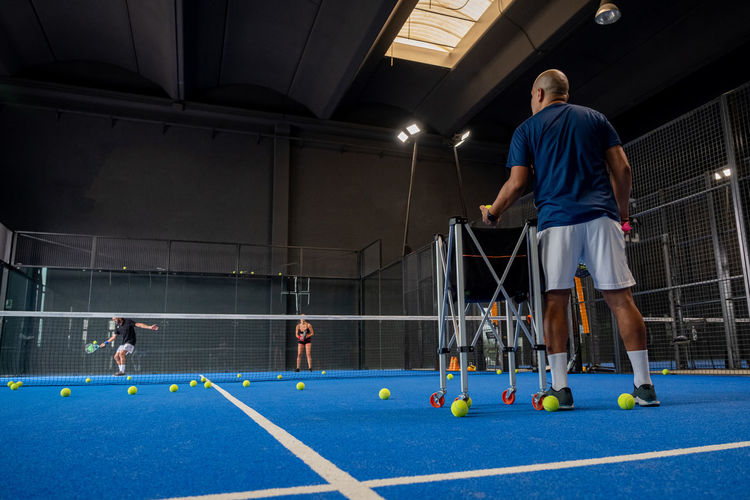 Monitor teaching padel class to man and woman, his students - trainer teaches how to play padel 