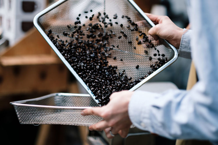 Midsection of barista preparing coffee beans in metal grate tray