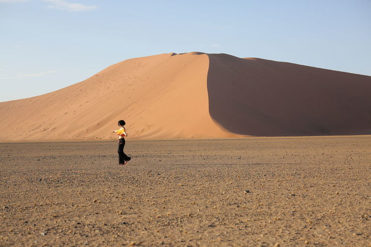 Woman walking on desert against sand dune