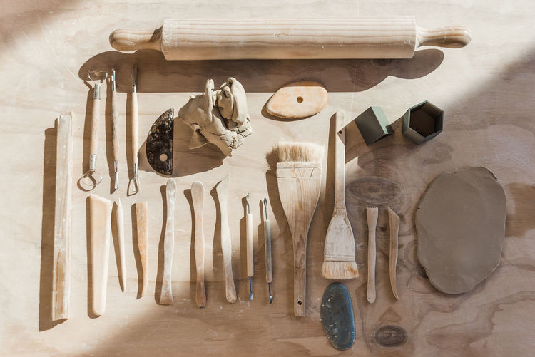 Top view of set of various tools for pottery with loops and stacks with paintbrushes and rolling pin with piece of smoothed clay placed on wooden table in workshop