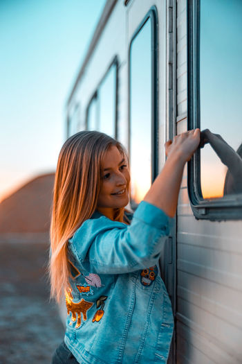 Side view of young woman standing by camper trailer