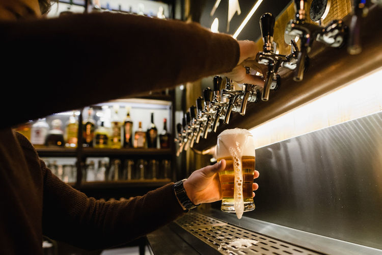 Cropped hands of bartender filling beer glass at bar