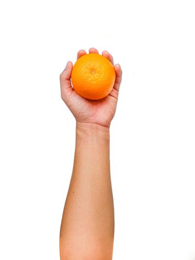 Cropped image of hand holding orange against white background