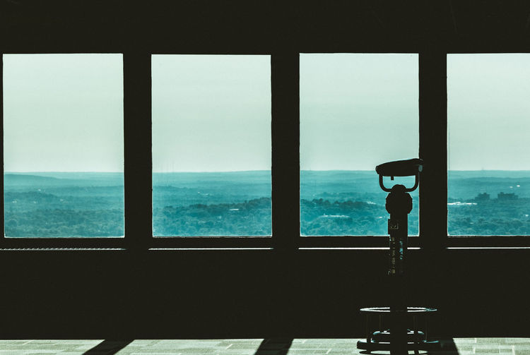 Silhouette man standing by sea against sky seen through window