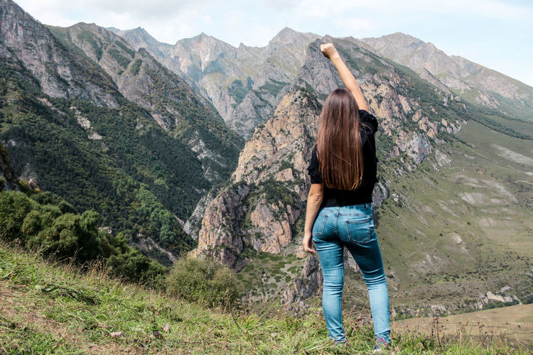 Rear view of woman with hand raised standing against mountains