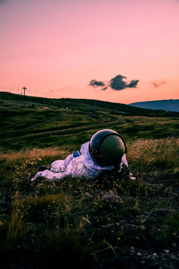 Rear view of woman sitting on grassy field against sky during sunset