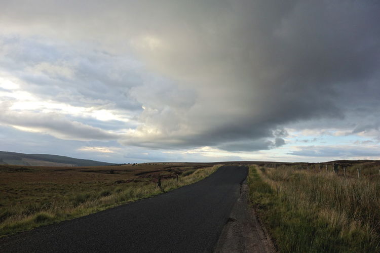 Empty road amidst field against sky