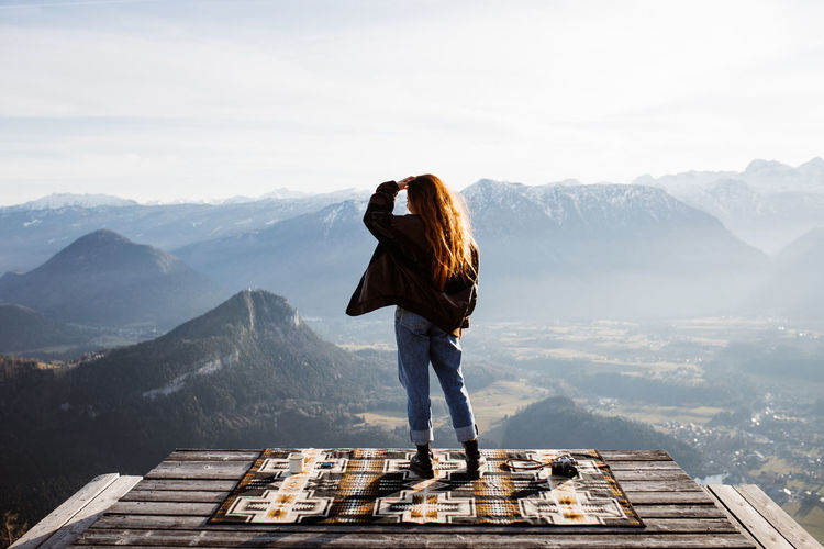 Back view of unrecognizable female tourist standing at viewpoint in mountains and observing amazing scenery in morning