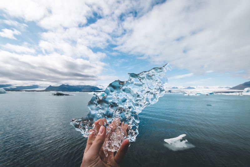 Cropped hand holding ice against sea