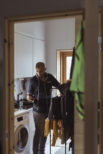 Man using smart phone while doing laundry chores in utility room