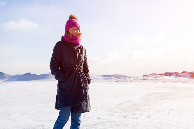 A young woman in a pink knitting hat, black coat enjoys winter nature, walking on the frozen sea 