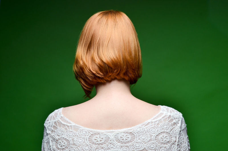 Redhead woman seen from behind with green background